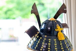 A close-up of a samurai helmet with a decorative tassel and a curved blade.