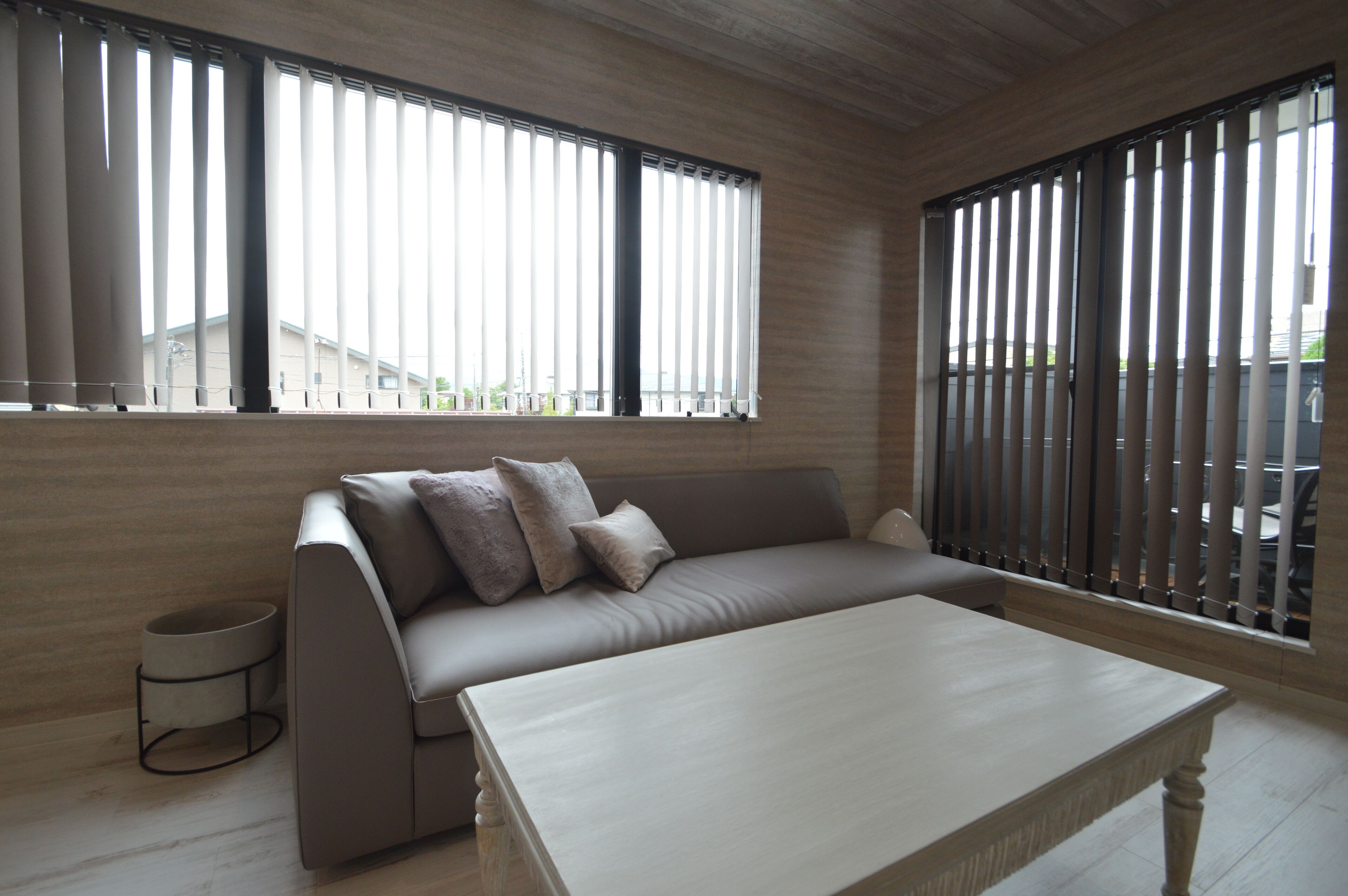 A modern living room with a beige sofa, a coffee table, and a window with vertical blinds.