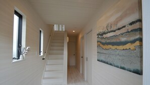 A hallway with a staircase, a painting on the wall, and a door at the end. - enico.Mt.Fuji peace (Fujikawaguchiko)