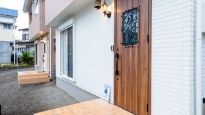 A building with a wooden door, a white brick exterior, and a small set of steps leading to the entrance. - Villa Hanasaku Fujikawaguchiko B (Fujikawaguchiko)
