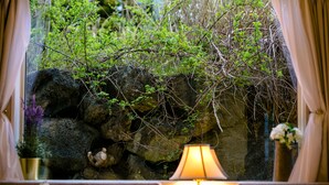A room with a large window overlooking a rocky garden with greenery. - Villa Hanasaku Fujikawaguchiko B (Fujikawaguchiko)