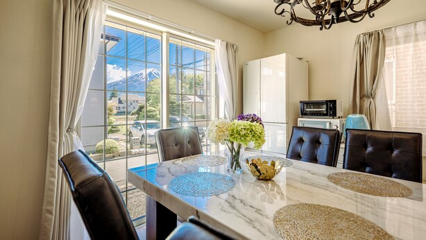 A dining area with a marble table, black leather chairs, a vase with flowers, and a view of mountains through large windows. - Villa Hanasaku Fujikawaguchiko B (Fujikawaguchiko)