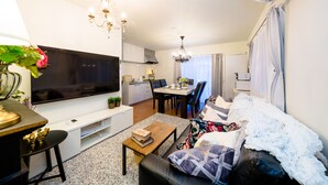 A modern living room with a flat-screen TV, a dining area with a table and chairs, and a cozy seating area with a sofa. - Villa Hanasaku Fujikawaguchiko B (Fujikawaguchiko)