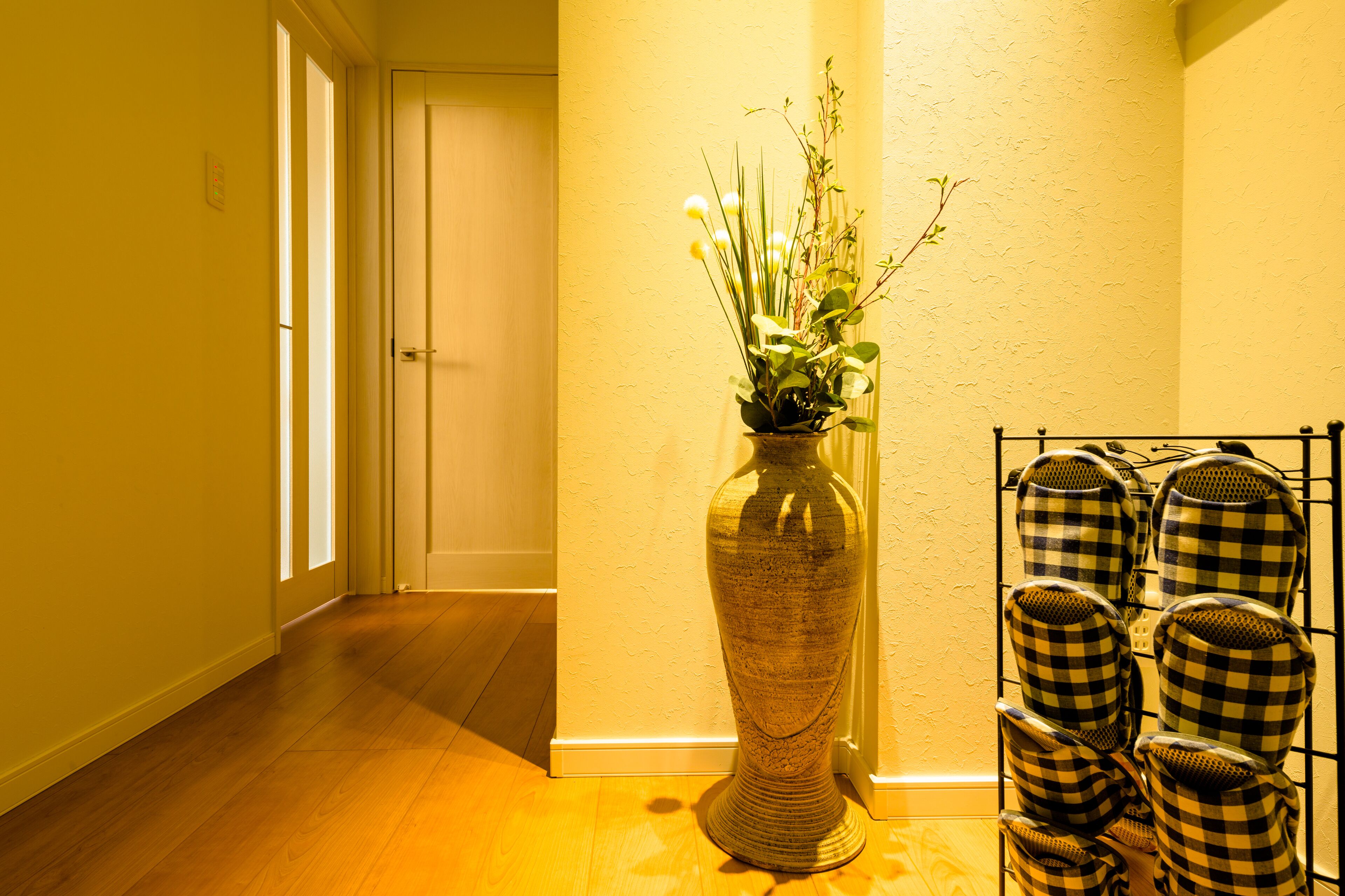 A hallway with a wooden floor, a vase with plants, and a rack of checkered mugs.