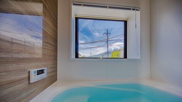 Een moderne badkamer met een groot bad, een raam met uitzicht op hoogspanningslijnen en een berg, en een thermostaat aan de muur.