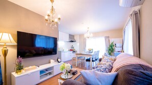 Een moderne woonkamer met een flatscreen televisie, een bank, een salontafel en een eethoek op de achtergrond.