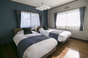 A hotel room with two beds, a nightstand, a lamp, and large windows with curtains. - Villa Yawaragi (Fujikawaguchiko)