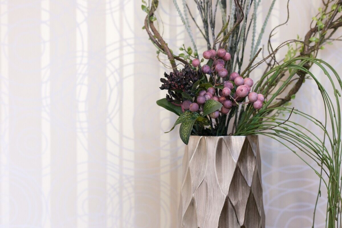 A decorative vase with a geometric design containing purple berries and green foliage.