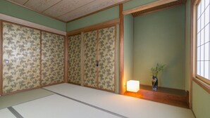Ein traditioneller japanischer Raum mit Tatami-Bodenbelag, Shoji-Schirmen und einem kleinen Tisch mit Lampe und Pflanze.