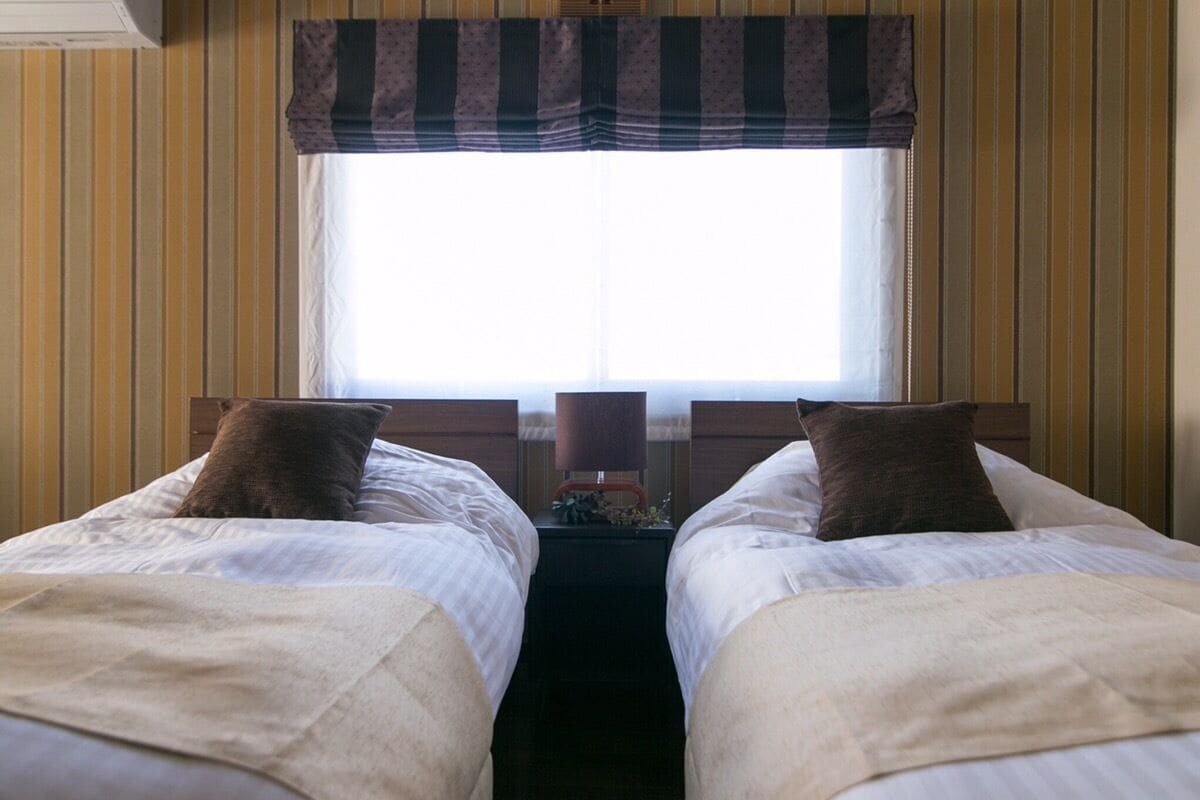 Ein Hotelzimmer mit zwei Einzelbetten, einem Fenster mit einem gestreiften Vorhang und gestreifter Tapete.
