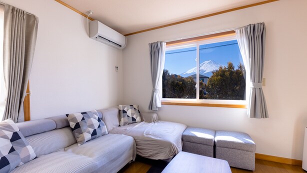 A room with a bed, a sofa, a small table, and a window with a view of a mountain.