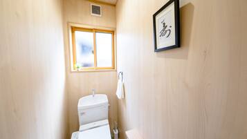 A small, wooden-finished bathroom with a toilet, a window, and a framed picture on the wall.