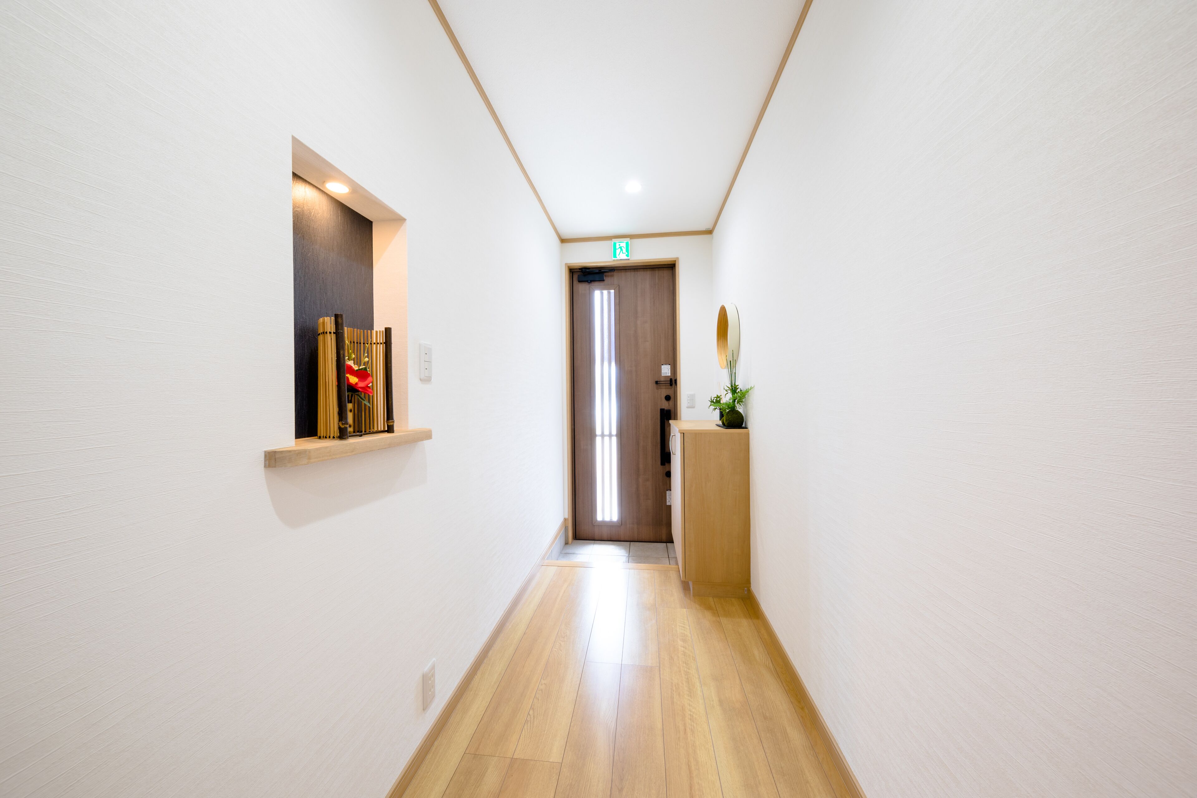 A narrow hallway with wooden flooring, white walls, and a door at the end.