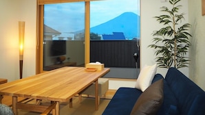 A room with a wooden table, a blue sofa, and a view of a mountain. - Mt. Fuji Akatsuki Kuu (Fujikawaguchiko)