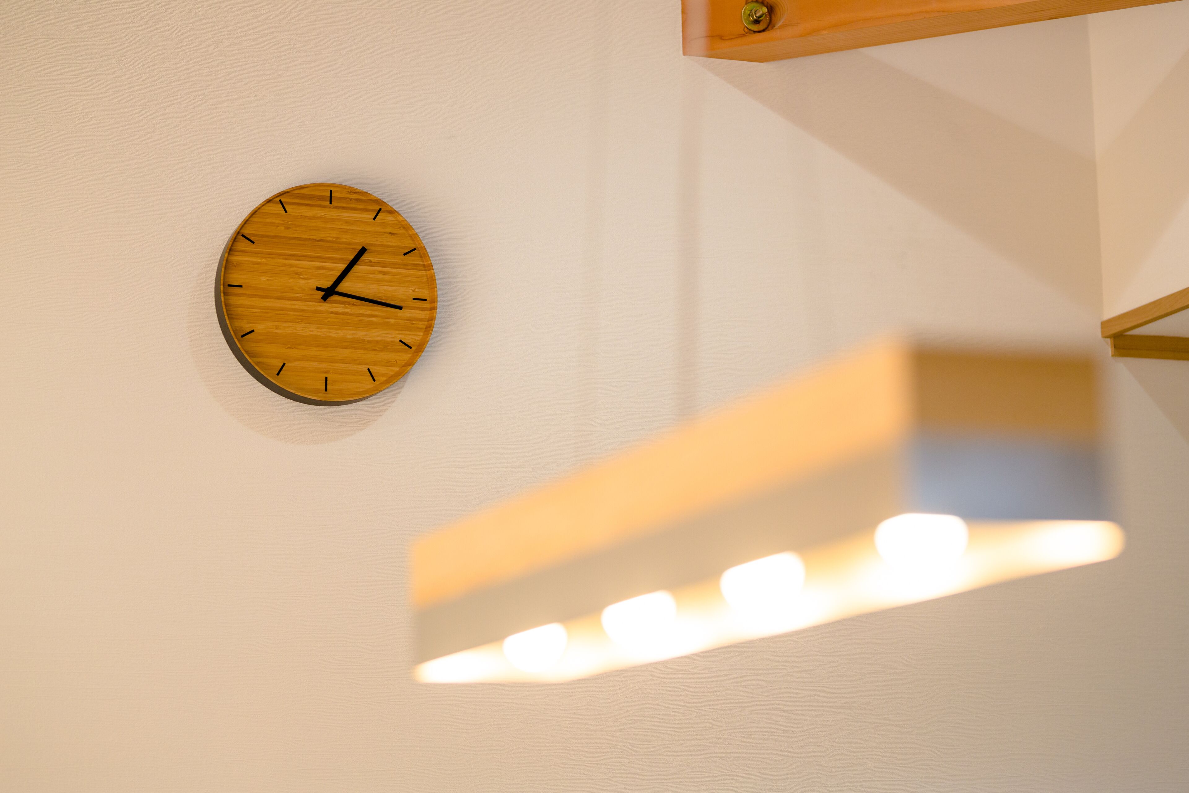 A wooden wall clock with a minimalist design, mounted on a plain wall.