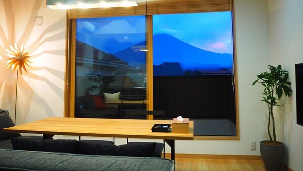 A modern living room with a large window, a wooden dining table, a sofa, and a potted plant. - Mt. Fuji Akatsuki Enn (Fujikawaguchiko)