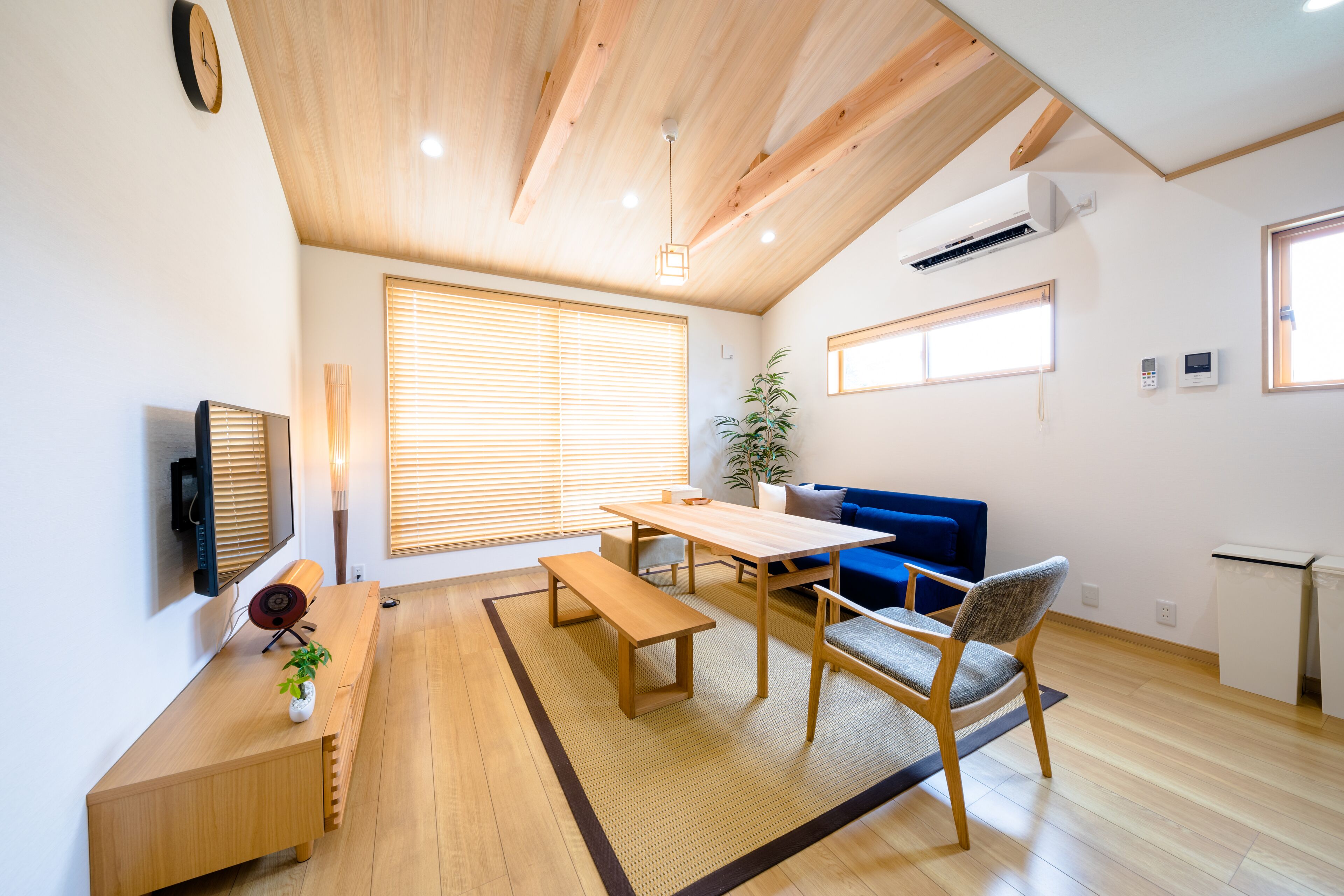 A modern living room with a wooden ceiling, a blue sofa, a wooden dining table, and a bench.