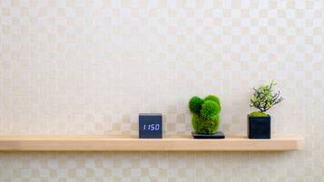 A shelf with a digital clock displaying 1150, a small potted plant, and a decorative item against a tiled wall.