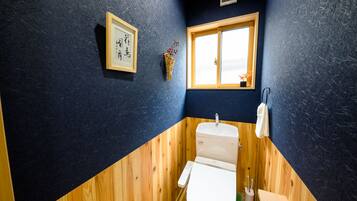 A bathroom with a wooden vanity, a white toilet, a framed artwork on the wall, and a window with a view of the sky.