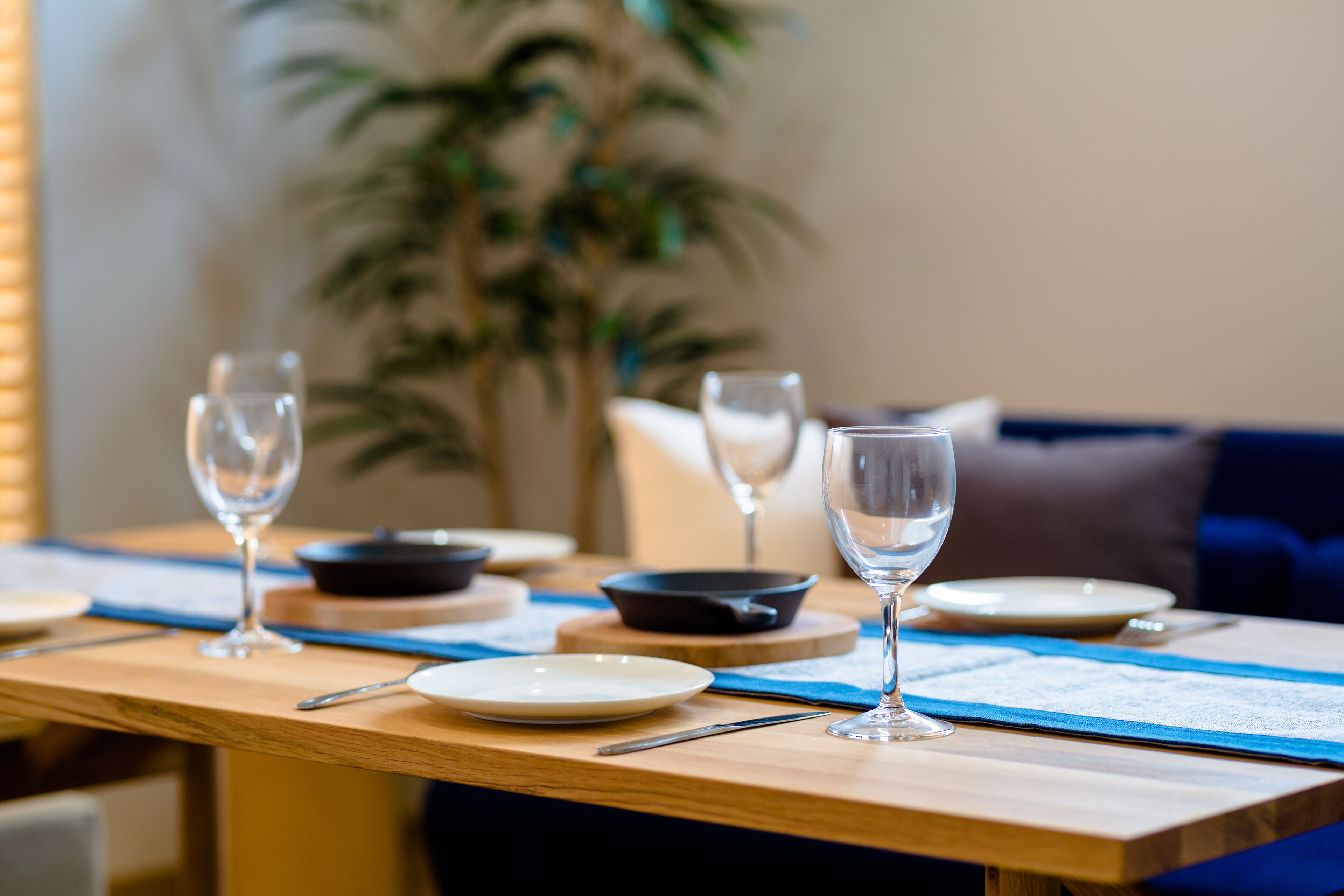 Una mesa de comedor dispuesta con platos, tazones y copas de vino, con un posavasos azul y una carta.