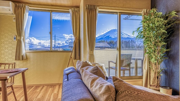 A room with a sofa, a dining table, and a large window offering a view of a mountain.