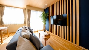 A modern living room with a sofa, a flat-screen TV mounted on a wall, a wooden floor, and a potted plant.