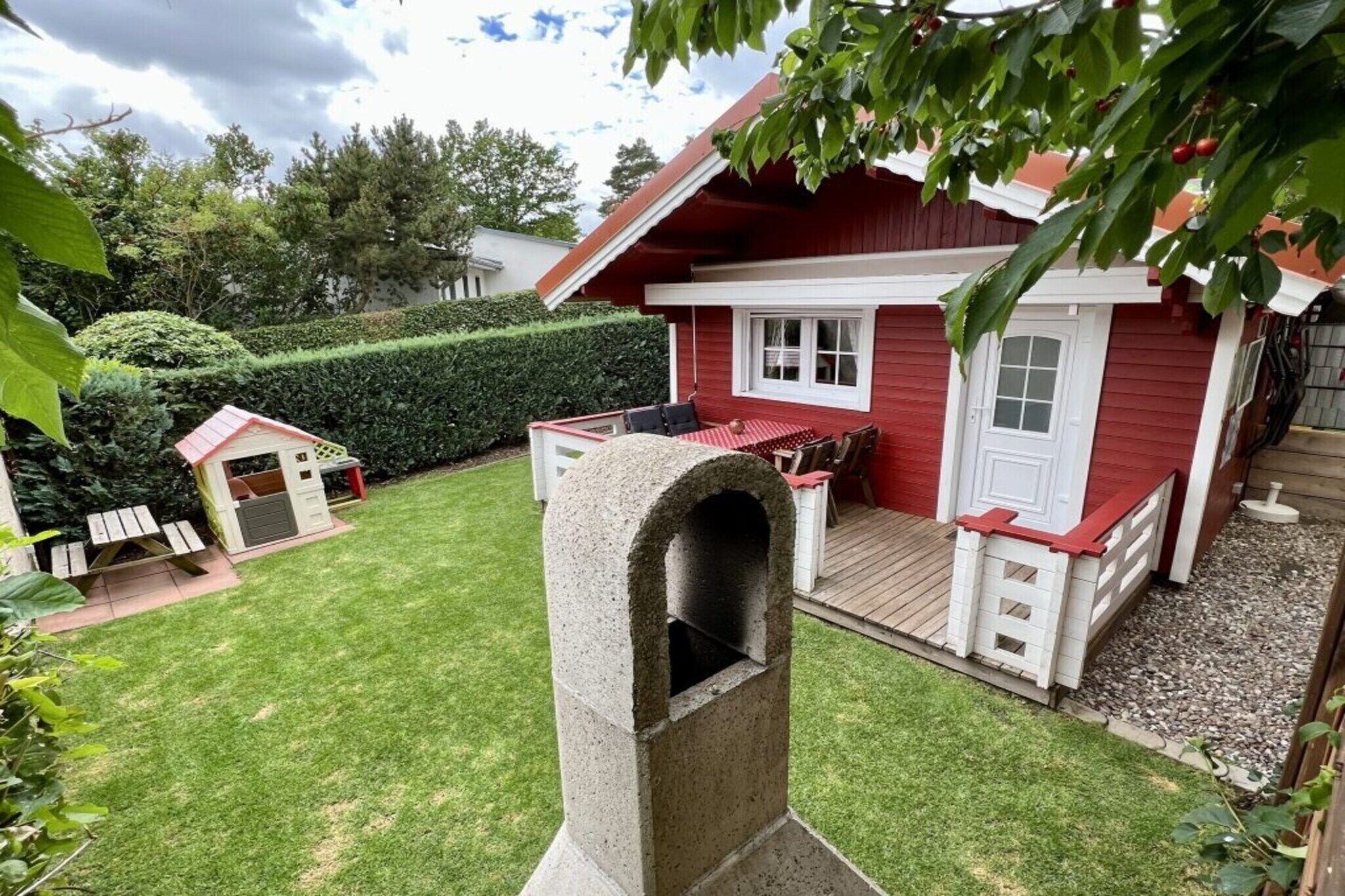 Ett rött hus med en liten trädgård, ett lekstuga och en stenugn.