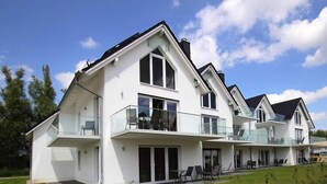 A modern two-story house with a balcony, large windows, and a well-maintained lawn.