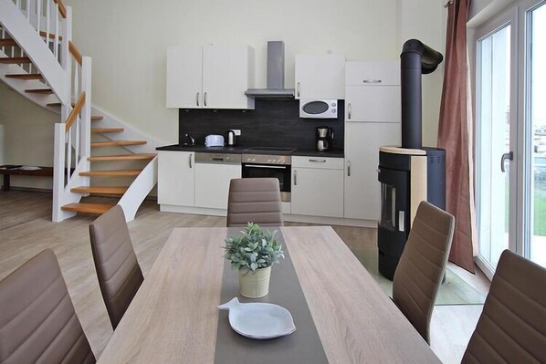 A modern kitchen with white cabinets, a black countertop, and a built-in stove. There is a dining table with chairs and a potted plant.