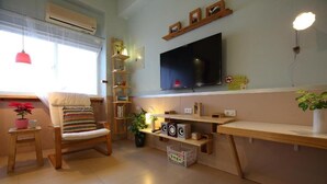 A living room with a TV, shelves, a chair, and a small table with a plant. - Huxi B&B (Ji'an)