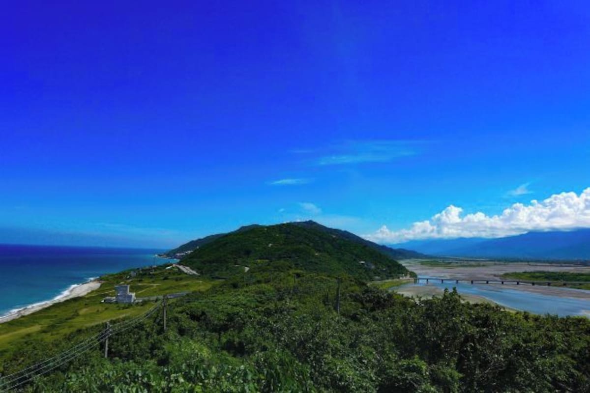 A coastal landscape with a mountain, a beach, and a bridge.