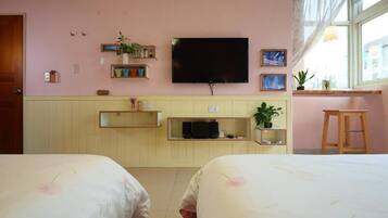 A room with two beds, a TV, shelves with plants, and a window with a view.
