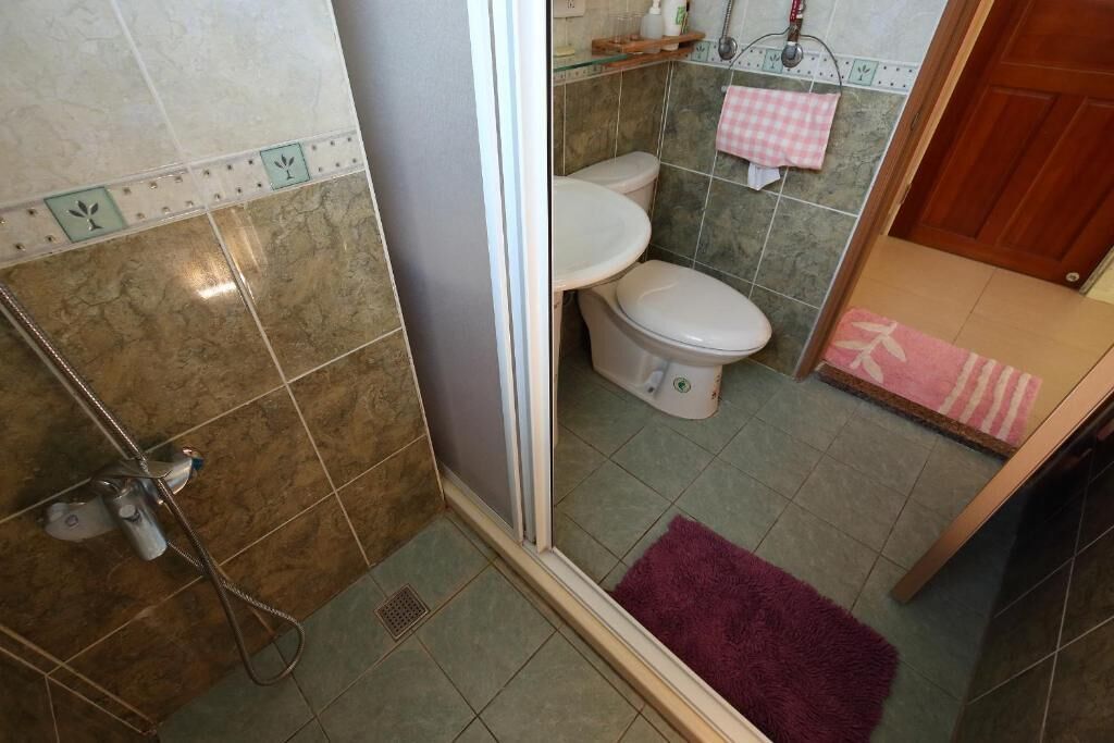 A bathroom with a shower, two toilets, and a pink and white checkered towel on the wall.