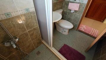 A bathroom with a shower, two toilets, and a pink and white checkered towel on the wall.