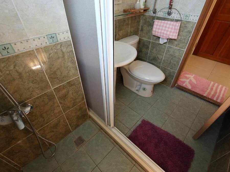 A bathroom with a shower, two toilets, and a pink and white checkered towel on the wall.
