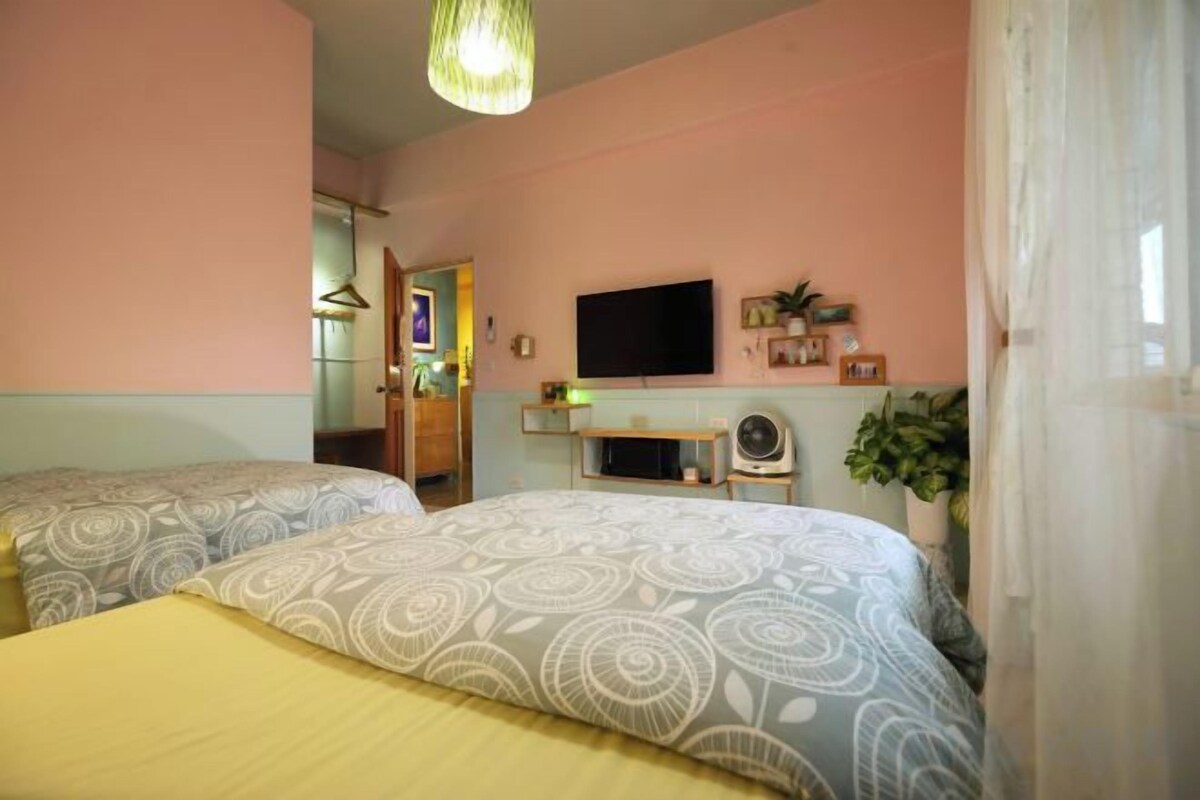A bedroom with two beds, a TV, a desk, and a plant.