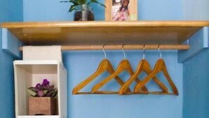 A room with a blue wall, a wooden shelf with a framed picture, and a wooden coat rack with hangers. - Huxi B&B (Ji'an)