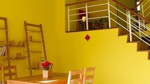A dining area with a wooden table and chairs, a staircase with a railing, and a yellow wall. - Huxi B&B (Ji'an)