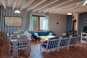 Ein Zimmer mit gestreifter Wandgestaltung, einem Esstisch mit Stühlen, einem blauen Sofa und einem Fernseher.