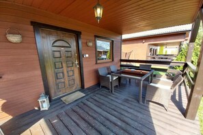 Une terrasse en bois avec une porte, une petite table avec des chaises et une lanterne suspendue.