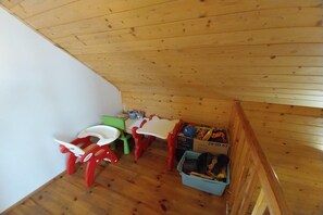 Une petite pièce mansardée aux murs en bois et au plafond en pente. On y trouve deux petites chaises pour enfants, une petite table et un bac de rangement bleu rempli de jouets.