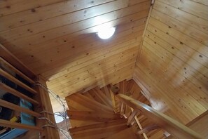 A wooden spiral staircase in a cabin with a light fixture at the top.