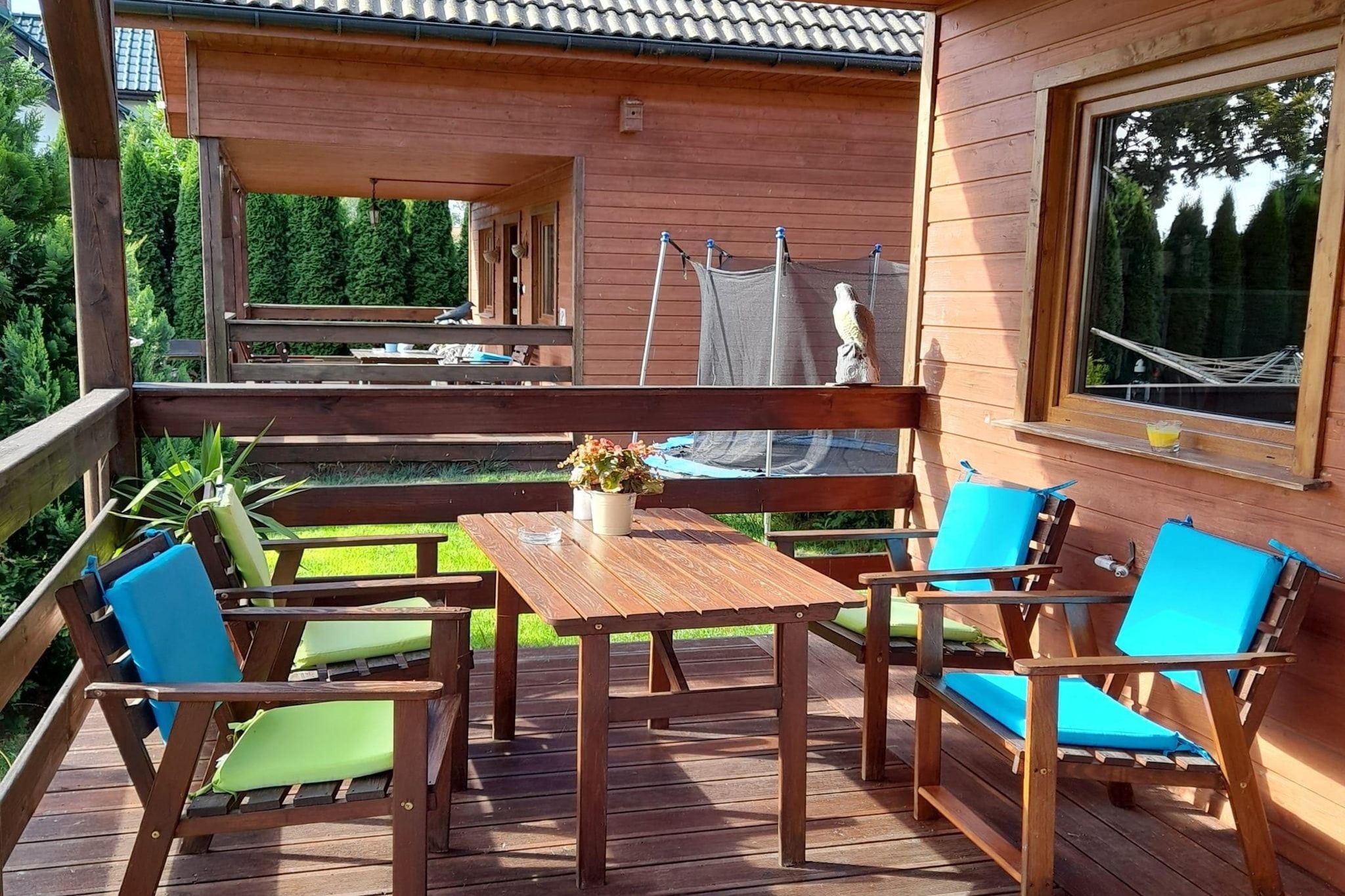 Una terraza de madera con mesa y sillas, un pequeño jardín y vista a una casa.