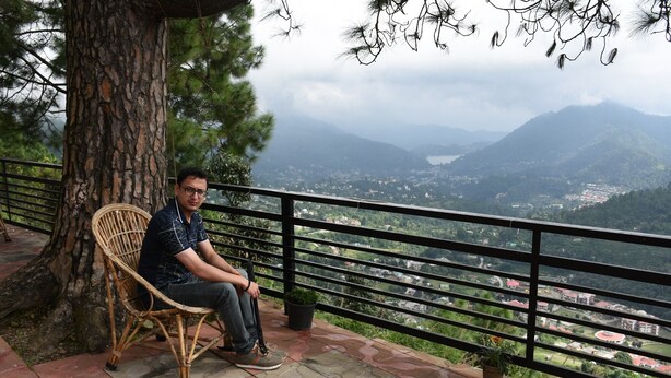 A man sitting on a wicker chair by a railing overlooking a valley. - The Moksha Heights (Nainital)