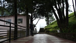 A pathway with a metal railing, leading to a building with a pink facade and a window. - The Moksha Heights (Nainital)