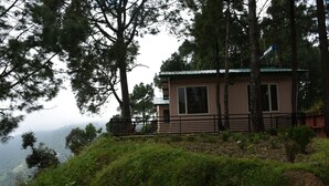 A two-story building with a balcony, surrounded by dense trees and a hillside. - The Moksha Heights (Nainital)