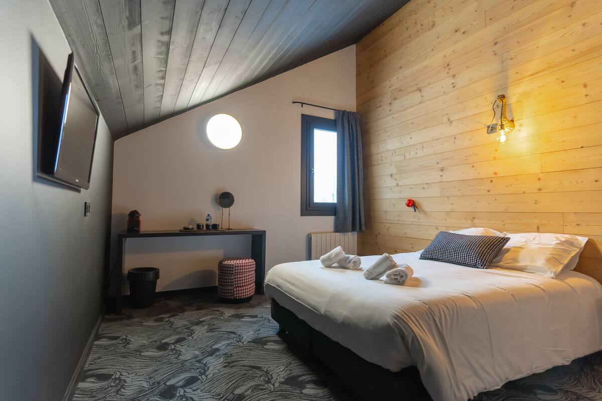 Quarto com cama, mesa de cabeceira, espelho, janela e luminária fixada na parede.