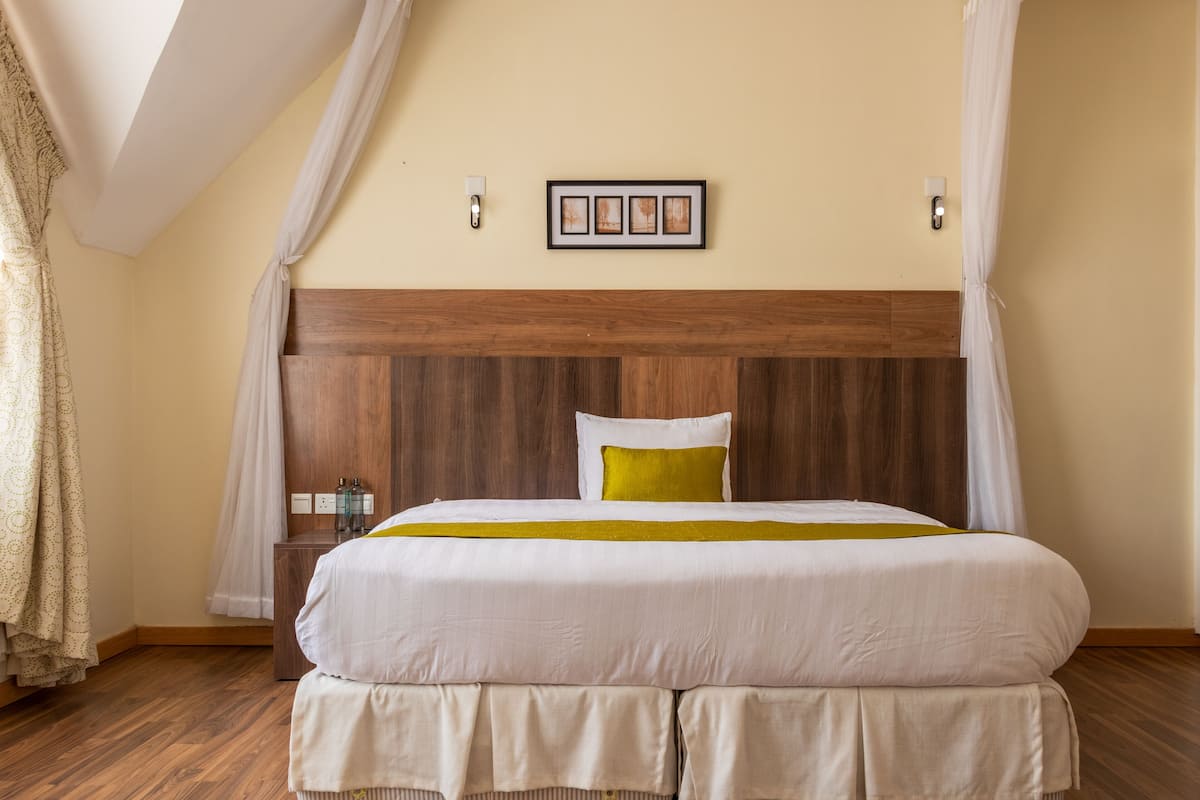 A large bed with a wooden headboard, a bedside table with bottles, and a wall-mounted picture frame.