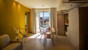 Una sala de estar moderna con comedor, un sofá, un sillón colorido y vistas al mar a través de amplios ventanales.