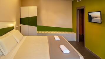 A hotel room with a bed, a wardrobe, a bench, and a television on the wall.